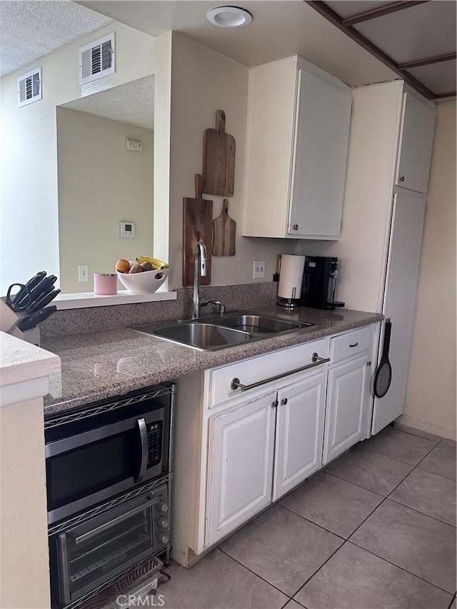 kitchen featuring stainless steel microwave, light tile patterned flooring, sink, white cabinetry, and a textured ceiling