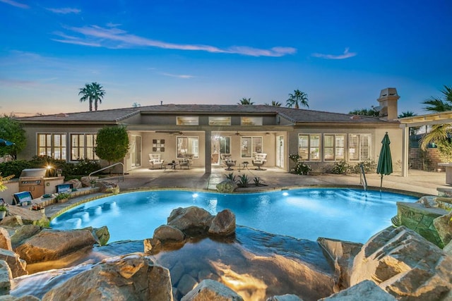 pool at dusk with ceiling fan and a patio area