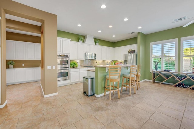 kitchen featuring stainless steel appliances, a breakfast bar, white cabinets, and a center island with sink