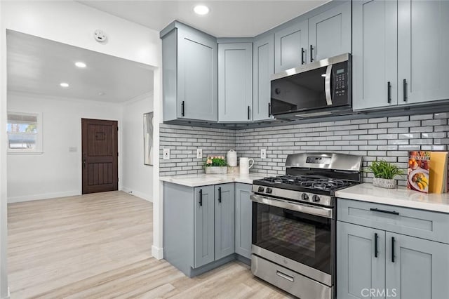 kitchen featuring gray cabinets, backsplash, stainless steel appliances, light hardwood / wood-style floors, and ornamental molding