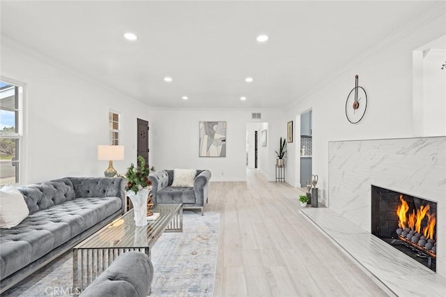 living room with crown molding, a premium fireplace, and light wood-type flooring