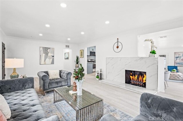 living room featuring ornamental molding, a high end fireplace, and light wood-type flooring