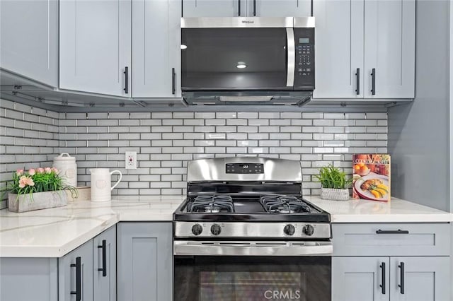 kitchen with tasteful backsplash, gray cabinets, light stone counters, and stainless steel gas stove