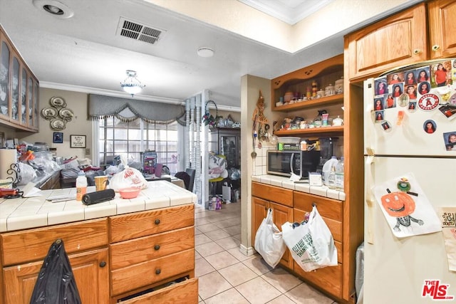 kitchen featuring white fridge, light tile patterned floors, tile countertops, and crown molding