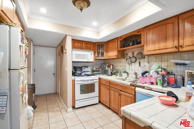 kitchen featuring tasteful backsplash, sink, a tray ceiling, white appliances, and tile counters