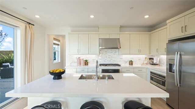 kitchen with exhaust hood, sink, white cabinetry, an island with sink, and stainless steel appliances