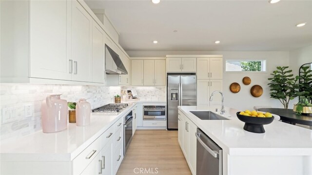 kitchen featuring a center island with sink, wall chimney range hood, white cabinets, appliances with stainless steel finishes, and sink