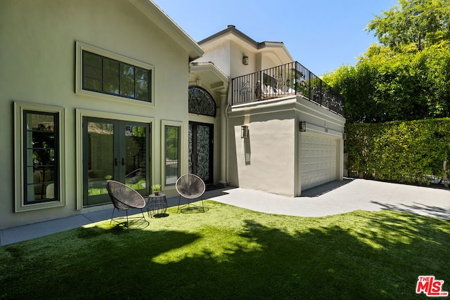 back of house featuring a lawn, french doors, a balcony, and a garage