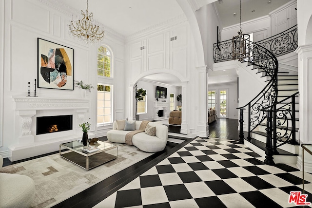 living room with a towering ceiling, crown molding, french doors, a chandelier, and decorative columns