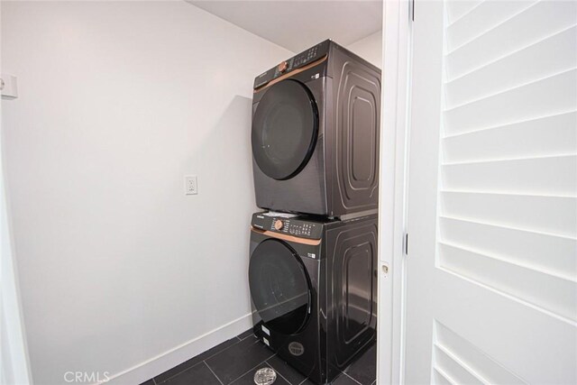 laundry area with stacked washer and dryer and dark tile patterned flooring