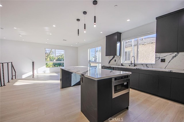 kitchen featuring sink, tasteful backsplash, a center island, hanging light fixtures, and light hardwood / wood-style flooring