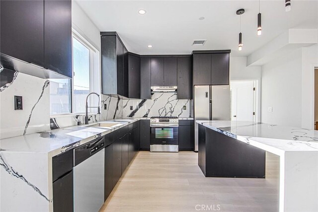 kitchen with light stone countertops, hanging light fixtures, stainless steel appliances, light hardwood / wood-style floors, and decorative backsplash