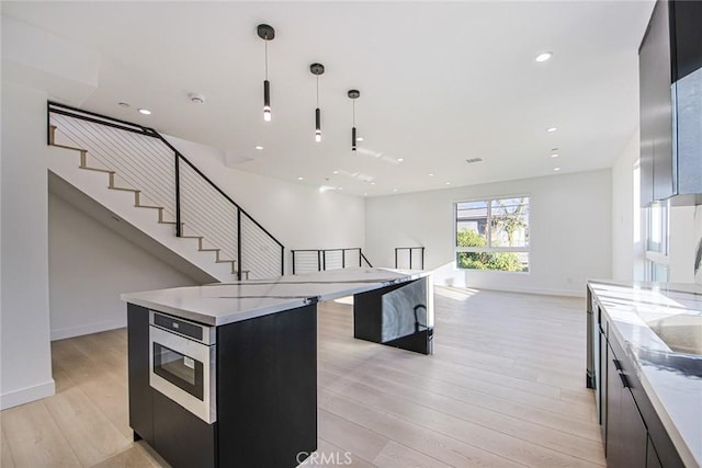 kitchen featuring stainless steel microwave, a kitchen island, light hardwood / wood-style flooring, hanging light fixtures, and light stone counters