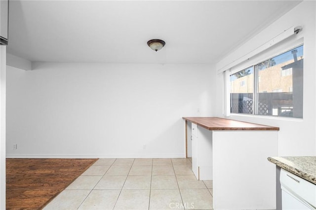 kitchen with light tile patterned floors, butcher block counters, white dishwasher, and white cabinetry