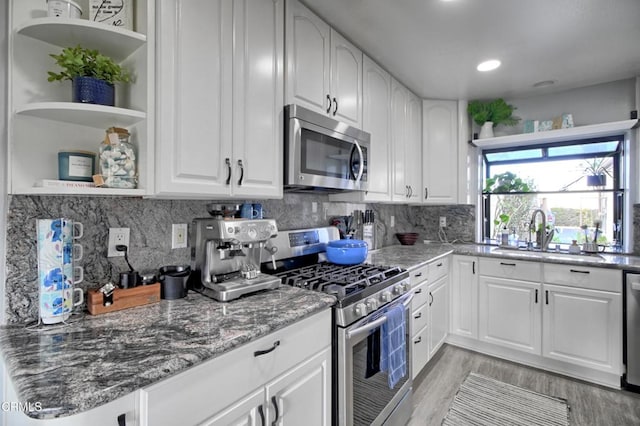 kitchen with white cabinets, appliances with stainless steel finishes, sink, and dark stone counters