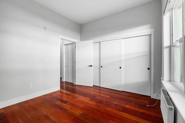 unfurnished bedroom featuring a closet, an AC wall unit, radiator heating unit, and dark hardwood / wood-style floors