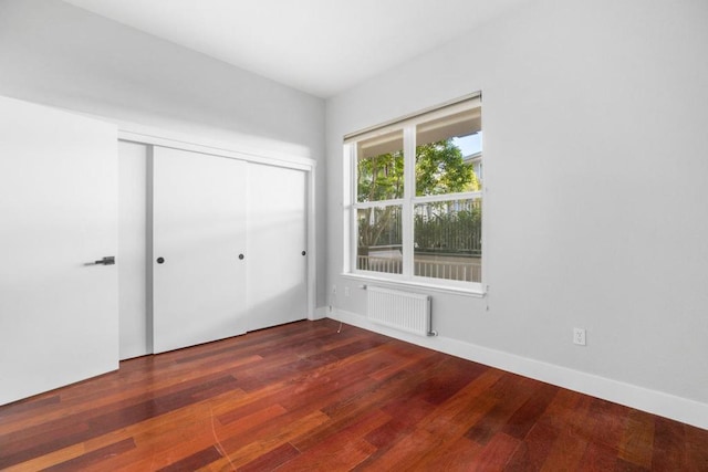 unfurnished bedroom featuring dark wood-type flooring, radiator heating unit, and a closet