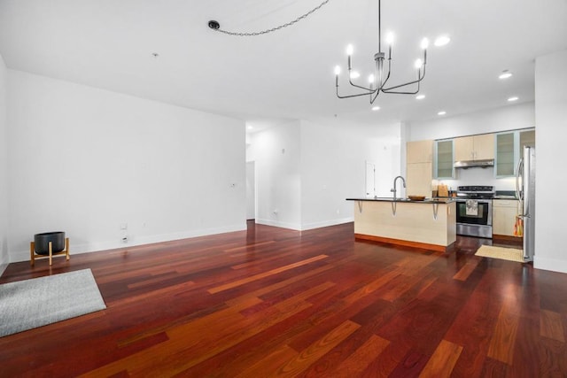 kitchen featuring dark wood-type flooring, a breakfast bar area, an inviting chandelier, a center island with sink, and appliances with stainless steel finishes