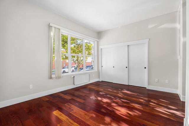 unfurnished bedroom with dark wood-type flooring, radiator heating unit, and a closet