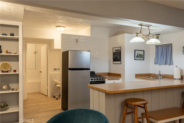 kitchen with light hardwood / wood-style floors, kitchen peninsula, a kitchen bar, stainless steel fridge, and sink