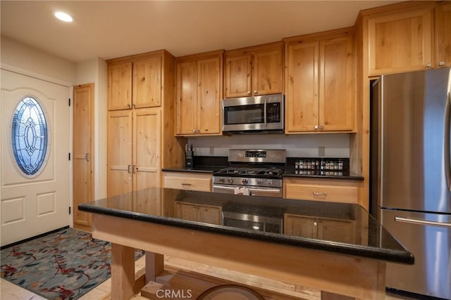 kitchen with light tile patterned floors, stainless steel appliances, dark stone countertops, and a kitchen bar