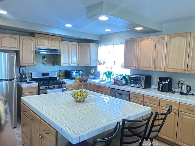 kitchen with sink, stainless steel appliances, a kitchen island, light brown cabinetry, and tile countertops