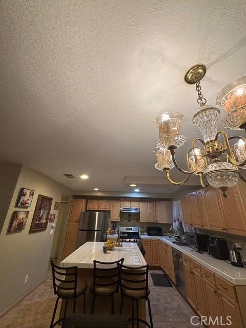 kitchen with appliances with stainless steel finishes, range hood, a center island, a textured ceiling, and tile countertops