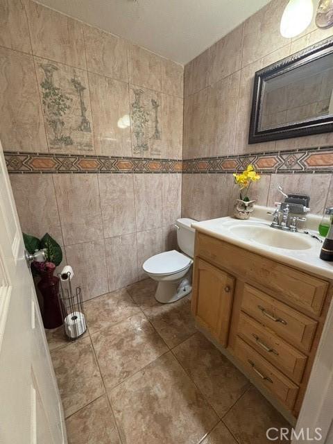 bathroom featuring vanity, tile patterned floors, tile walls, and toilet