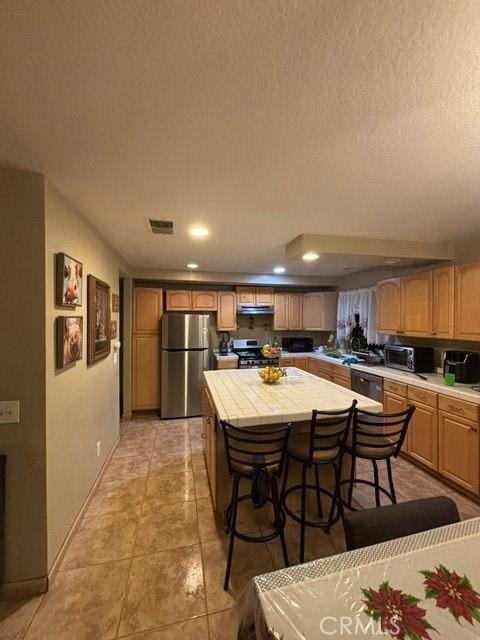 kitchen featuring a kitchen bar, extractor fan, tile countertops, a textured ceiling, and black appliances