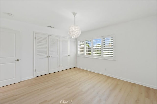 unfurnished bedroom featuring two closets, a chandelier, and light hardwood / wood-style flooring