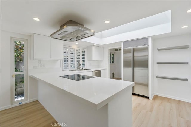 kitchen with kitchen peninsula, island exhaust hood, light wood-type flooring, white cabinetry, and appliances with stainless steel finishes