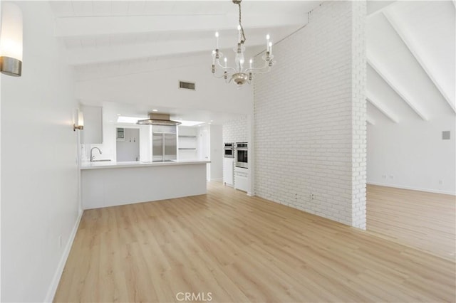 unfurnished living room with brick wall, light wood-type flooring, beam ceiling, and sink