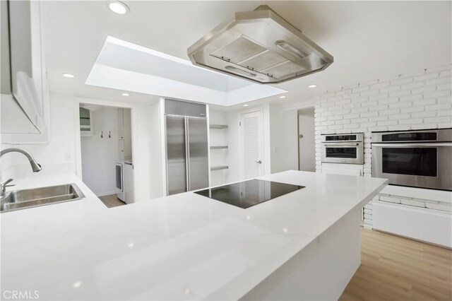 kitchen with stainless steel appliances, sink, light hardwood / wood-style flooring, kitchen peninsula, and extractor fan