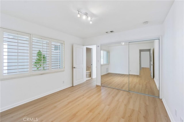 unfurnished bedroom featuring light wood-type flooring, a closet, and multiple windows