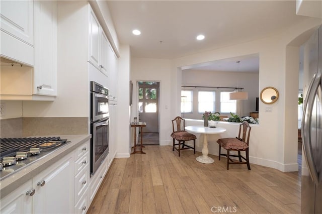 kitchen with hanging light fixtures, white cabinets, stainless steel appliances, and light hardwood / wood-style floors