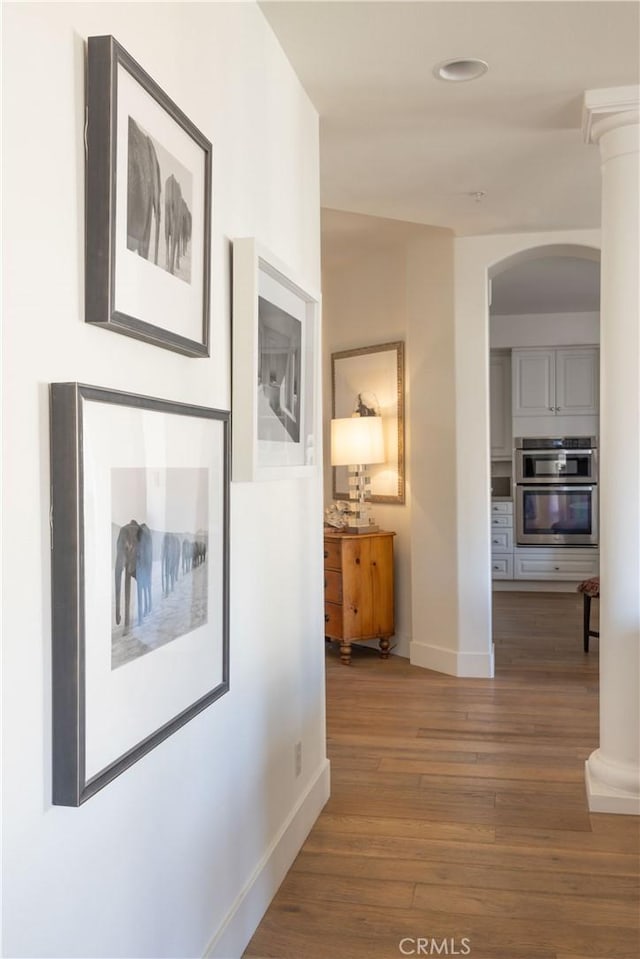 hallway with decorative columns and hardwood / wood-style flooring