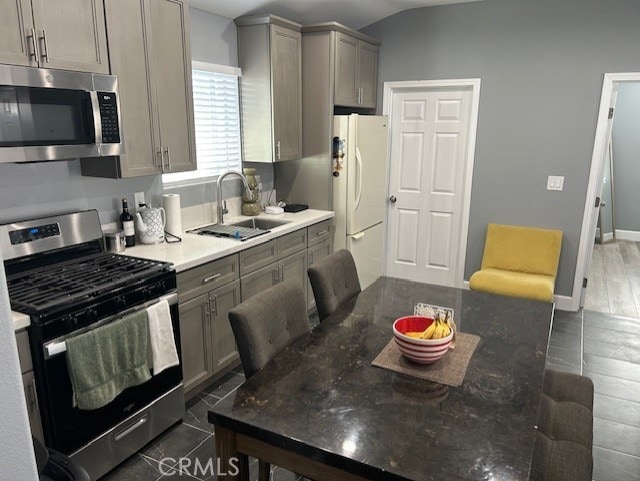 kitchen with stainless steel appliances, gray cabinets, a sink, and baseboards