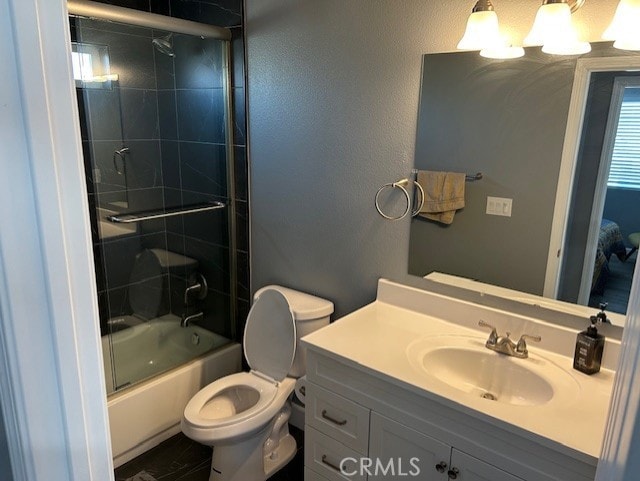 bathroom featuring a textured wall, vanity, toilet, and bath / shower combo with glass door