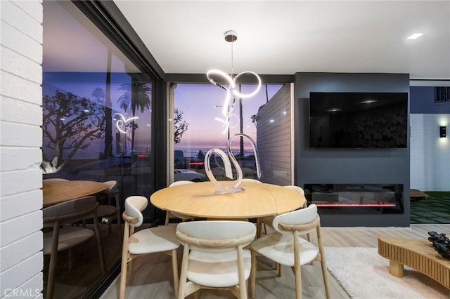 dining space featuring a glass covered fireplace, a notable chandelier, and wood finished floors