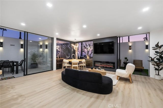 living area featuring a glass covered fireplace, recessed lighting, wood finished floors, and floor to ceiling windows