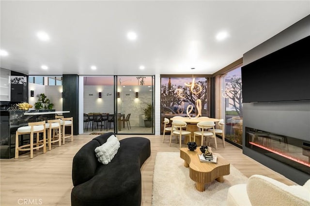 living area featuring wood finished floors, an inviting chandelier, recessed lighting, expansive windows, and a glass covered fireplace