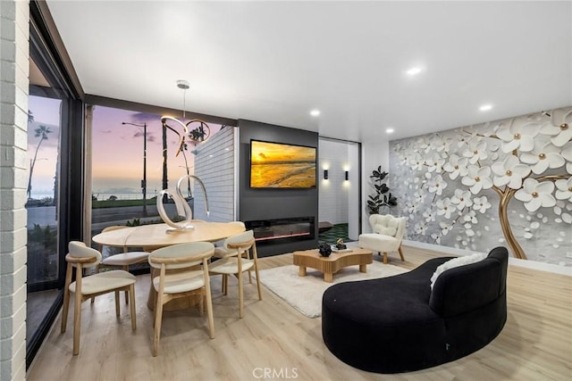 dining room with wallpapered walls, floor to ceiling windows, recessed lighting, wood finished floors, and a glass covered fireplace