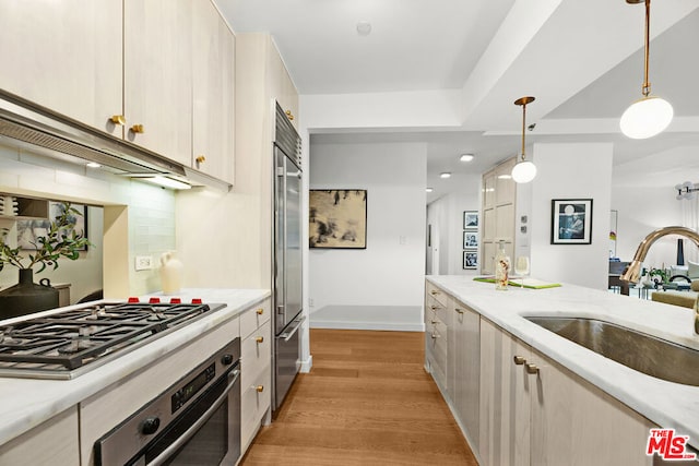 kitchen featuring backsplash, sink, light hardwood / wood-style flooring, hanging light fixtures, and stainless steel appliances