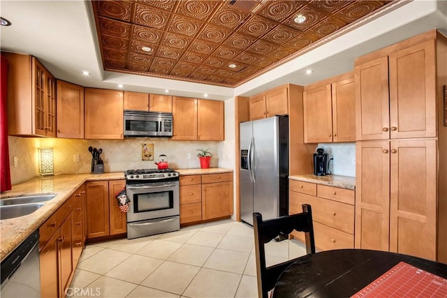 kitchen featuring backsplash, a tray ceiling, light stone countertops, stainless steel appliances, and light tile patterned floors