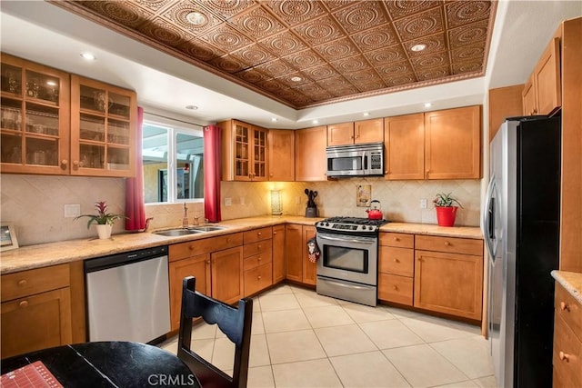 kitchen with appliances with stainless steel finishes, decorative backsplash, sink, a raised ceiling, and light tile patterned floors