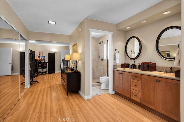 bathroom with toilet, vanity, tiled shower, and hardwood / wood-style floors