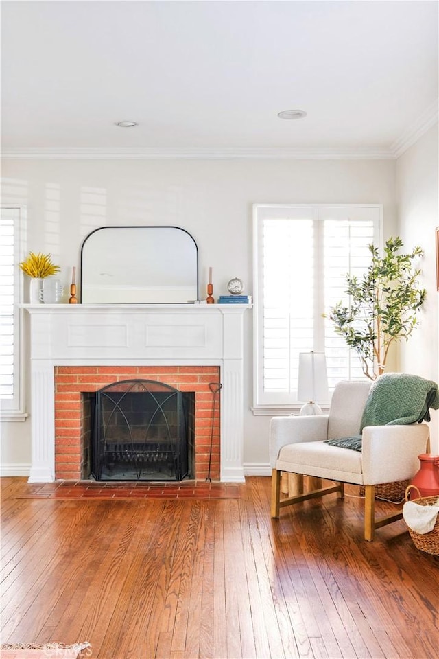 sitting room featuring a brick fireplace, hardwood / wood-style floors, crown molding, and a wealth of natural light