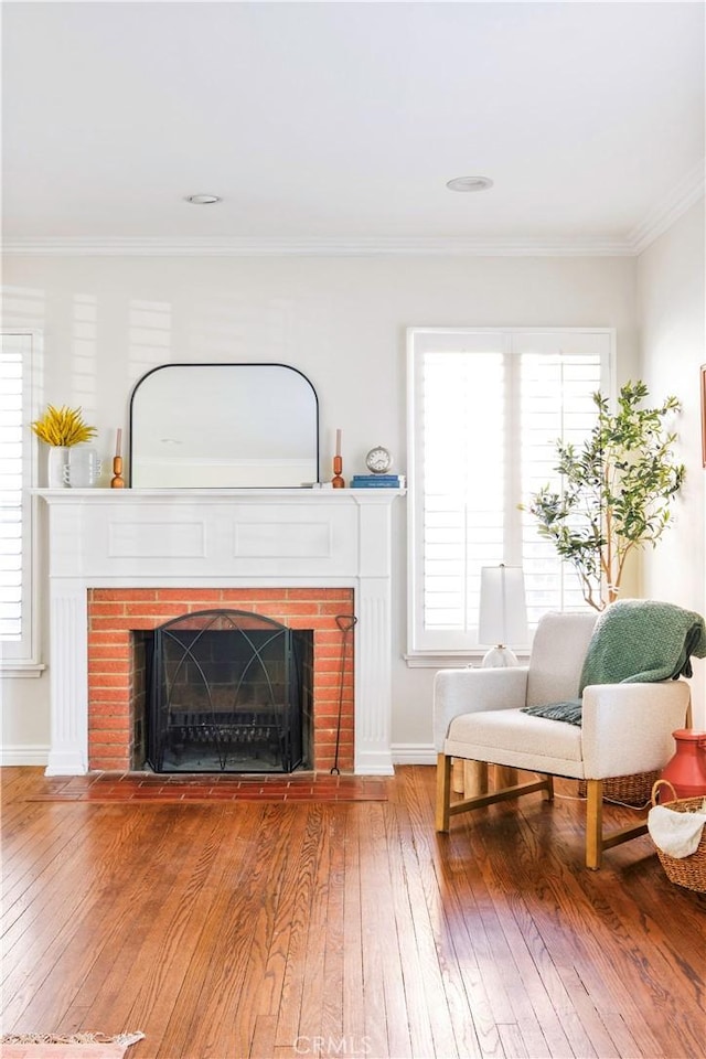 living area with ornamental molding, a fireplace, wood finished floors, and baseboards