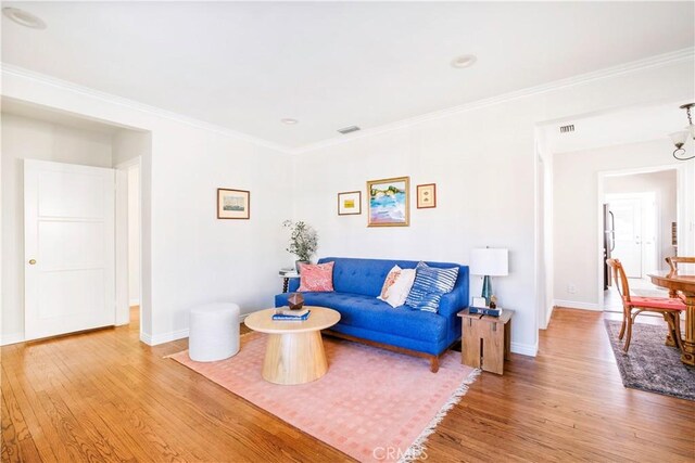 living room featuring ornamental molding, visible vents, baseboards, and wood finished floors