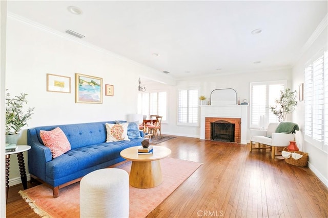 living room featuring a fireplace, wood finished floors, visible vents, baseboards, and crown molding